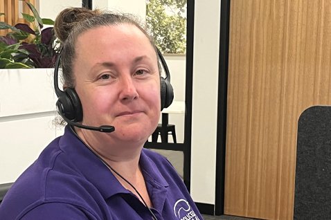 Photo of a person in an office. The person is wearing a stereo headset with a microphone.