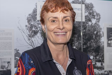 Photo of a person wearing an indigenous artwork QPS shirt. The background is a wall with a street scene image on it. 