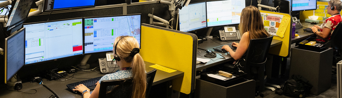 Woman Wearing Headphones in front of monitors in communication centre