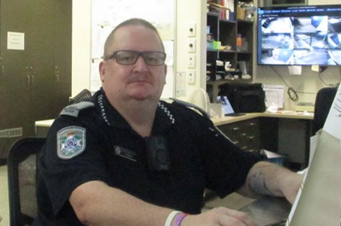 Photo of a person in a watchhouse officer uniform (very similar to the police officer uniform with different coloured epaulettes) sitting at a desk inside an office environment.