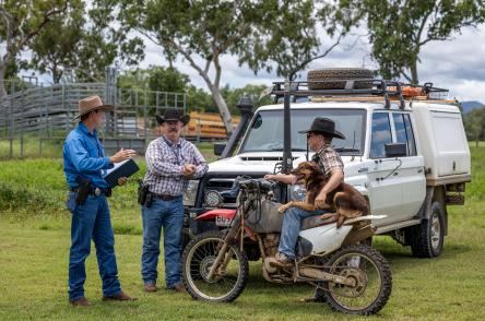 Farmer on motorbike with dog talks to plain clothes police officers in front of a police vehicle