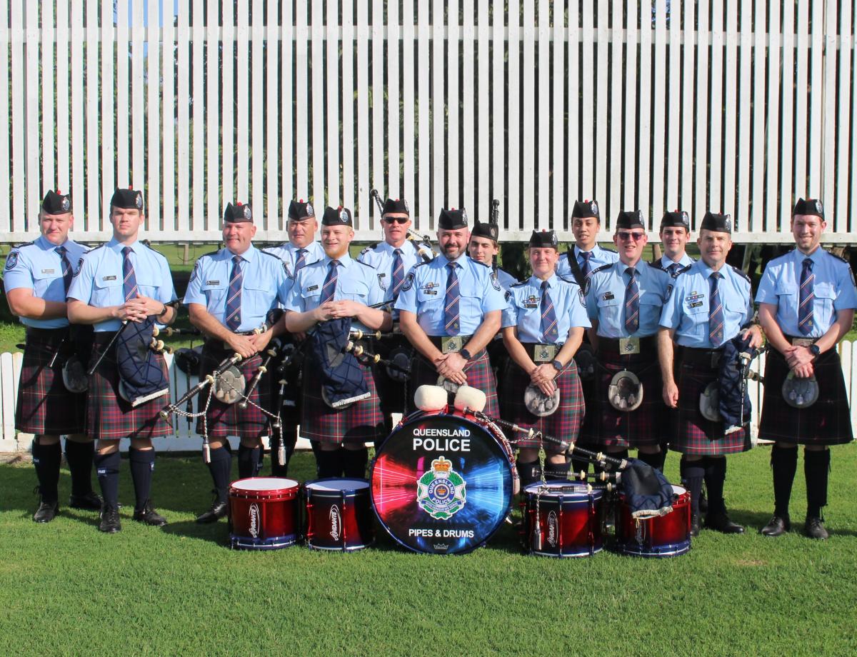 Queensland Police Pipes and Drums band standing in a line behind their drums.