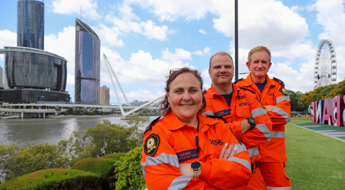 Three SES members on the South Bank of the Brisbane River, with casino, 1 George St and the ferris wheel in the background